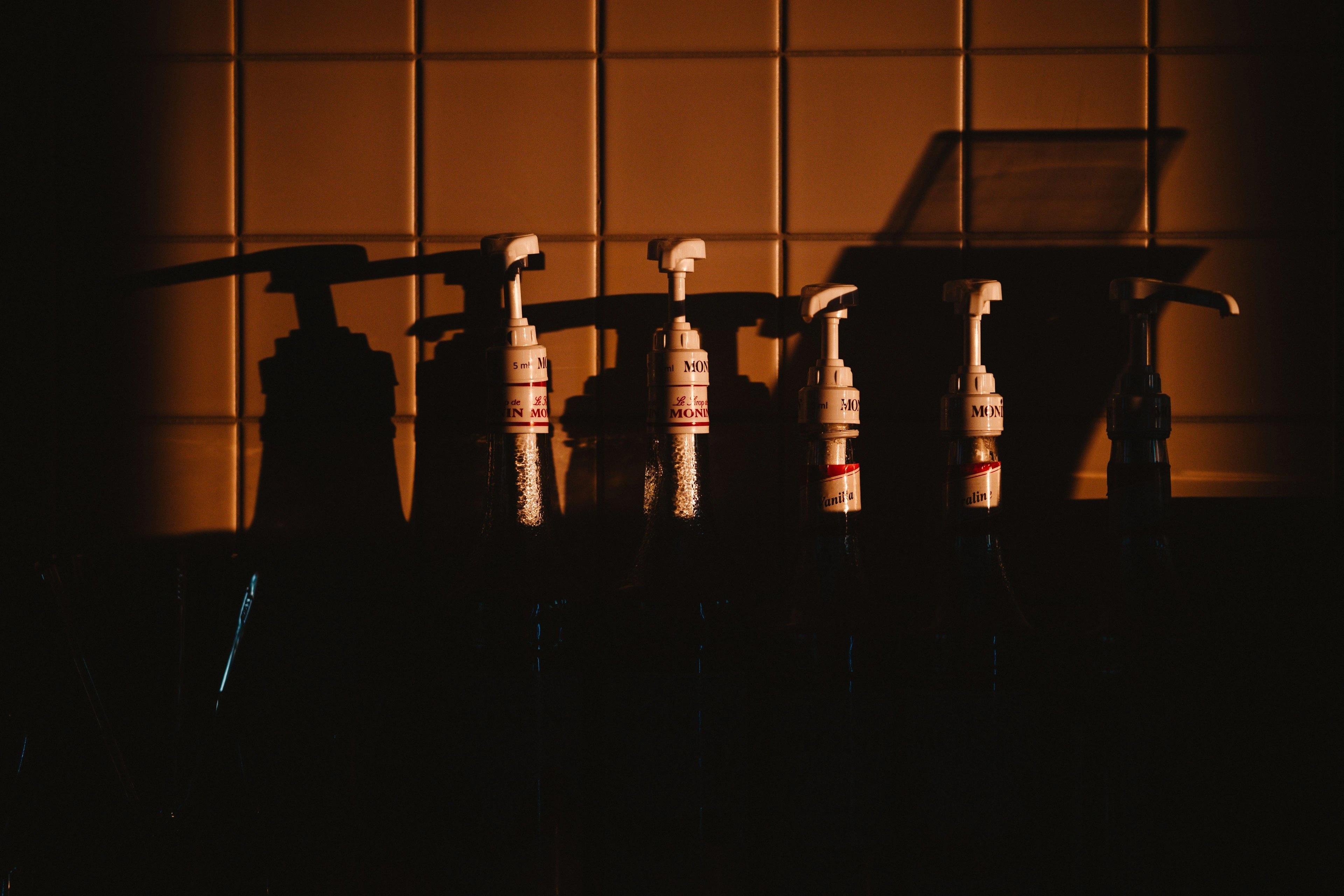 Pump bottles silhouetted against a warm backlit window in a dark room.
