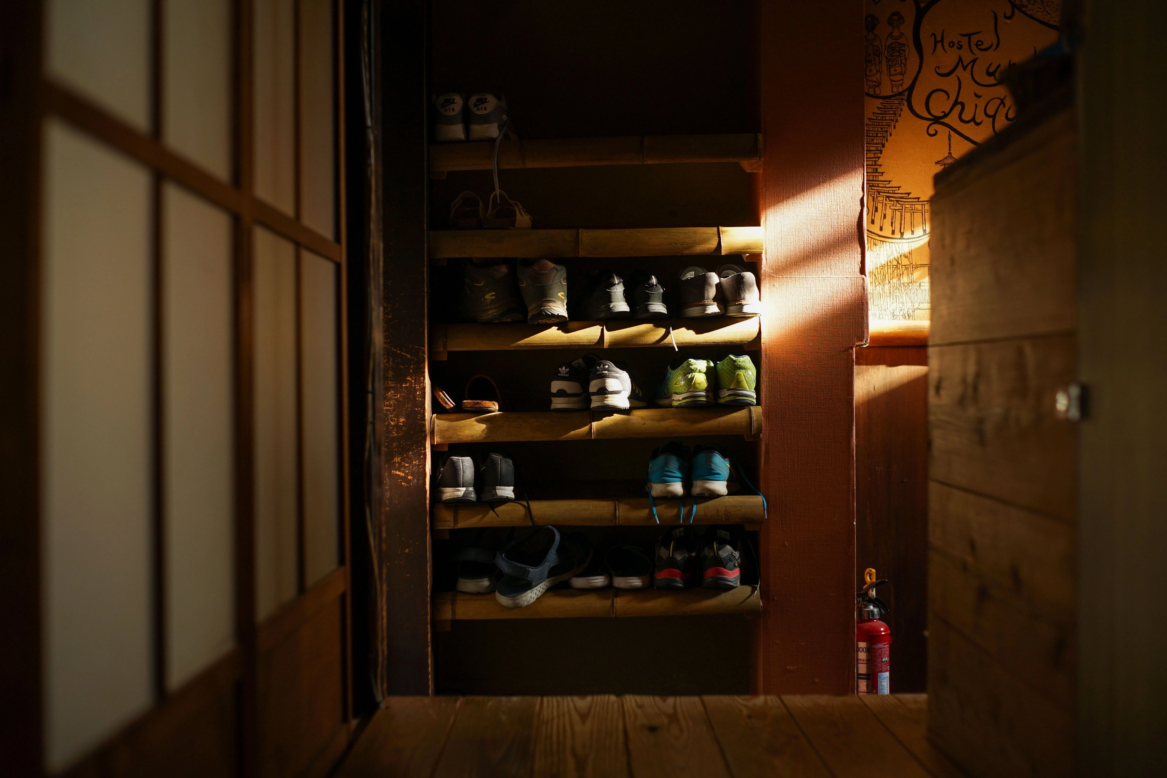 A warmly lit open shoe cupboard in a dark entryway.