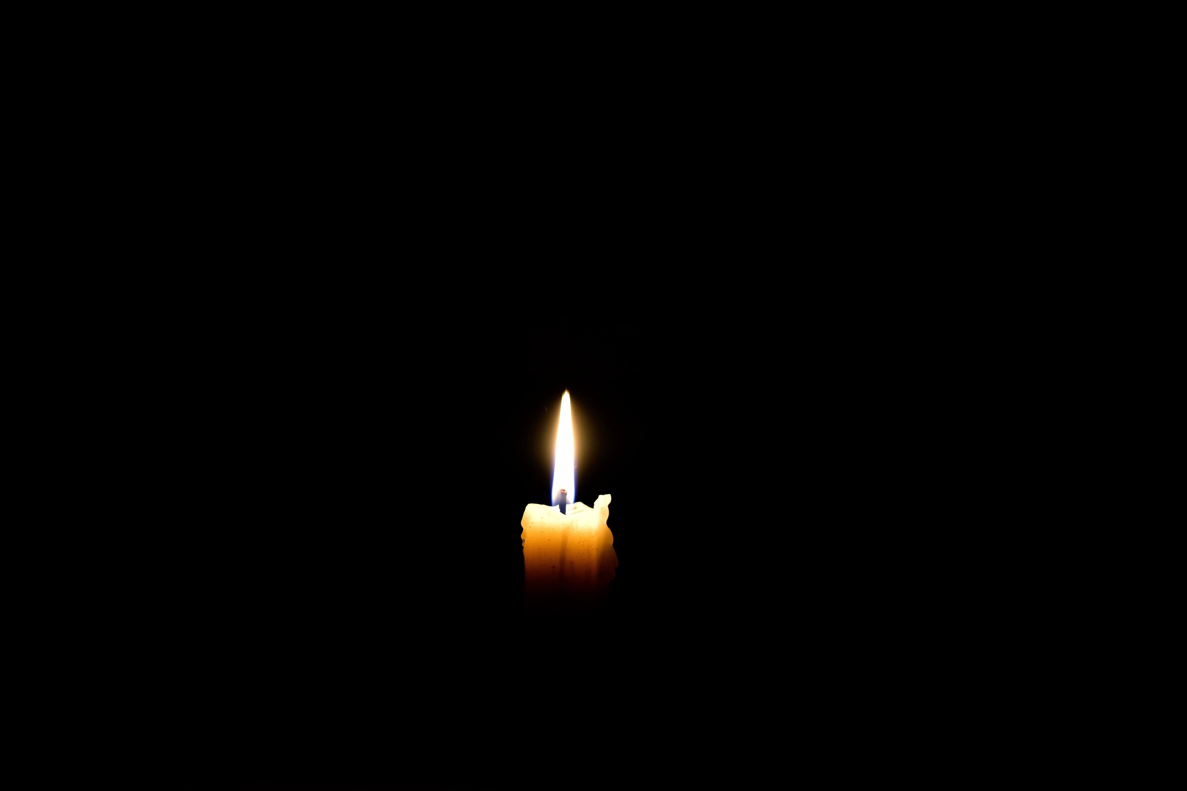 A single lit candle flame against a black background.