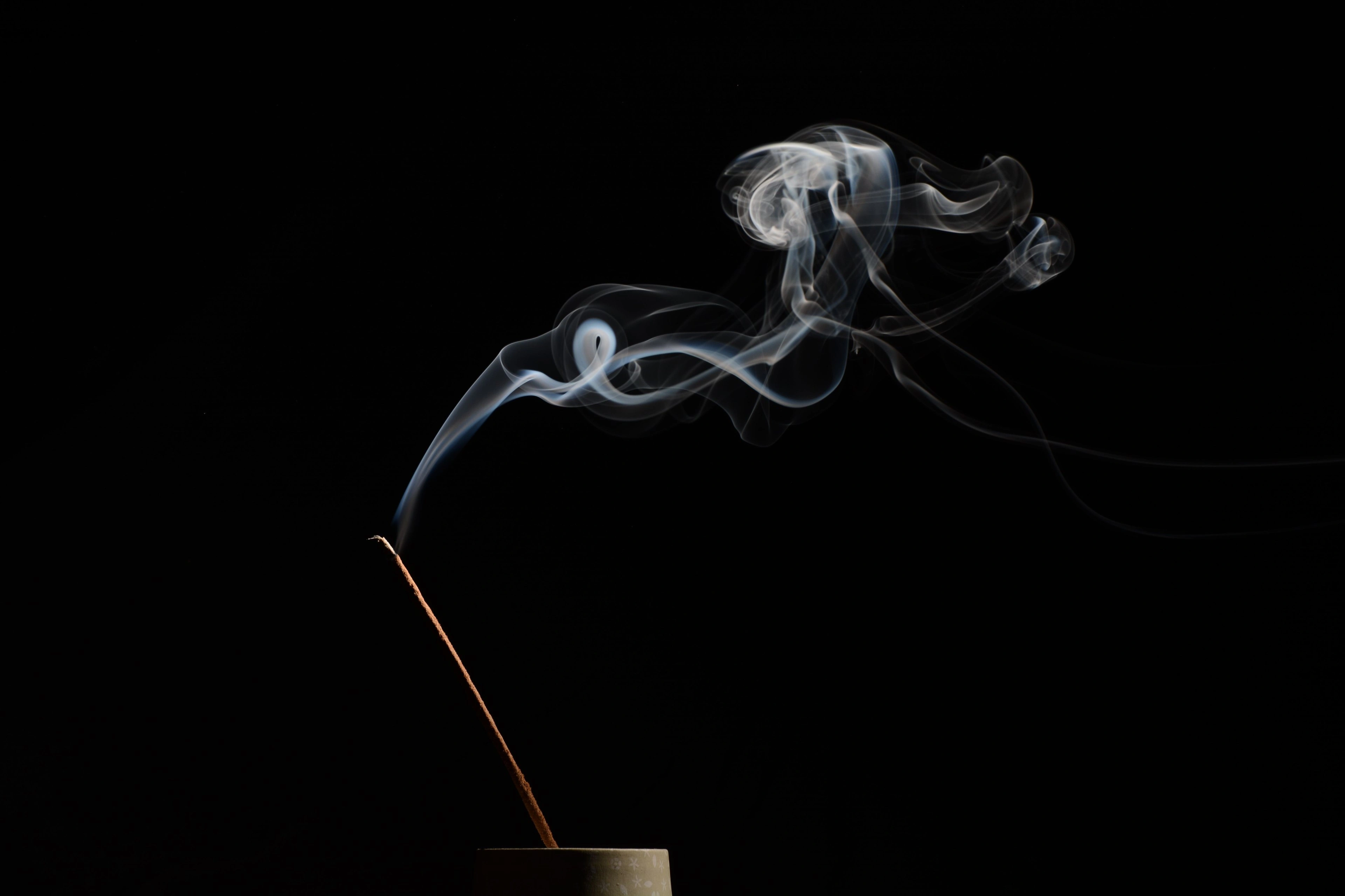 A thin ribbon of incense smoke rising in warm light against deep shadow.