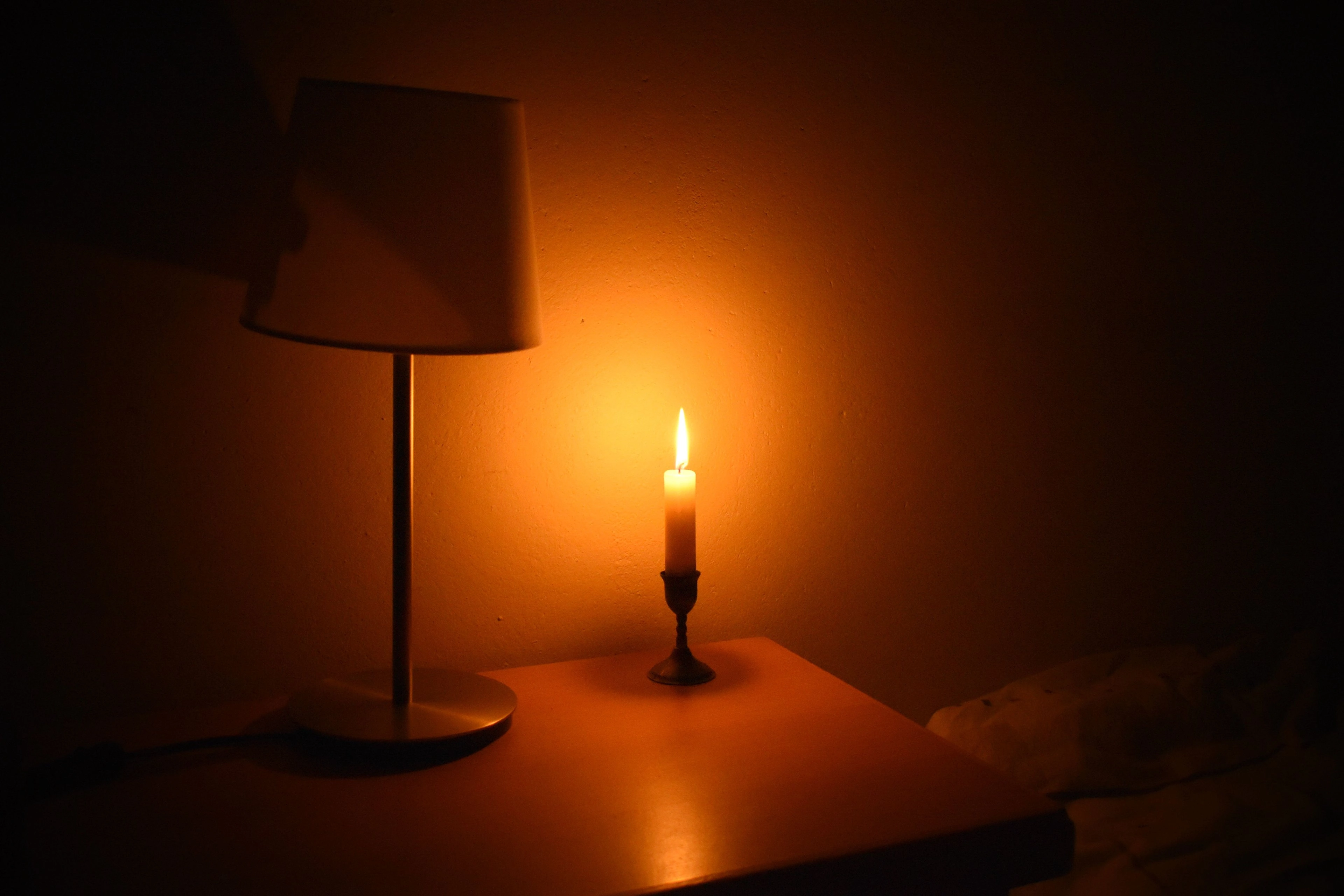 A warm table lamp and candle glowing on a dark nightstand.