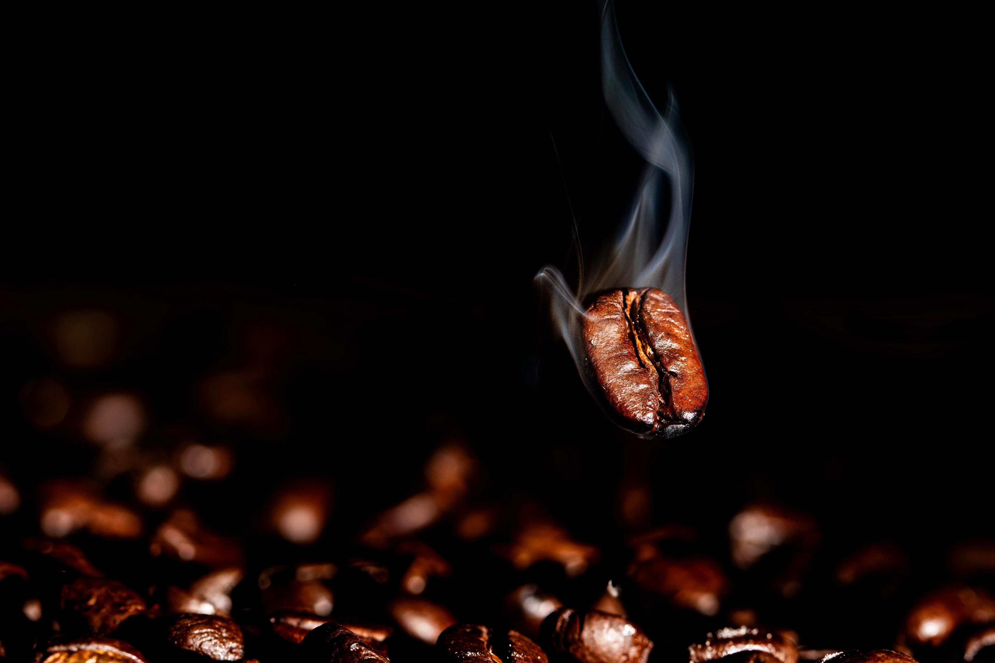 A hand holding a glass of dark tea with rising steam in warm low light.