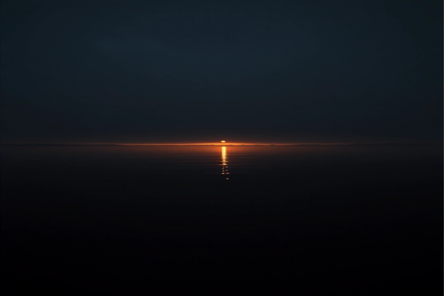 First light spilling over the horizon of a still lake at dawn with a deep amber gold reflection on obsidian water.