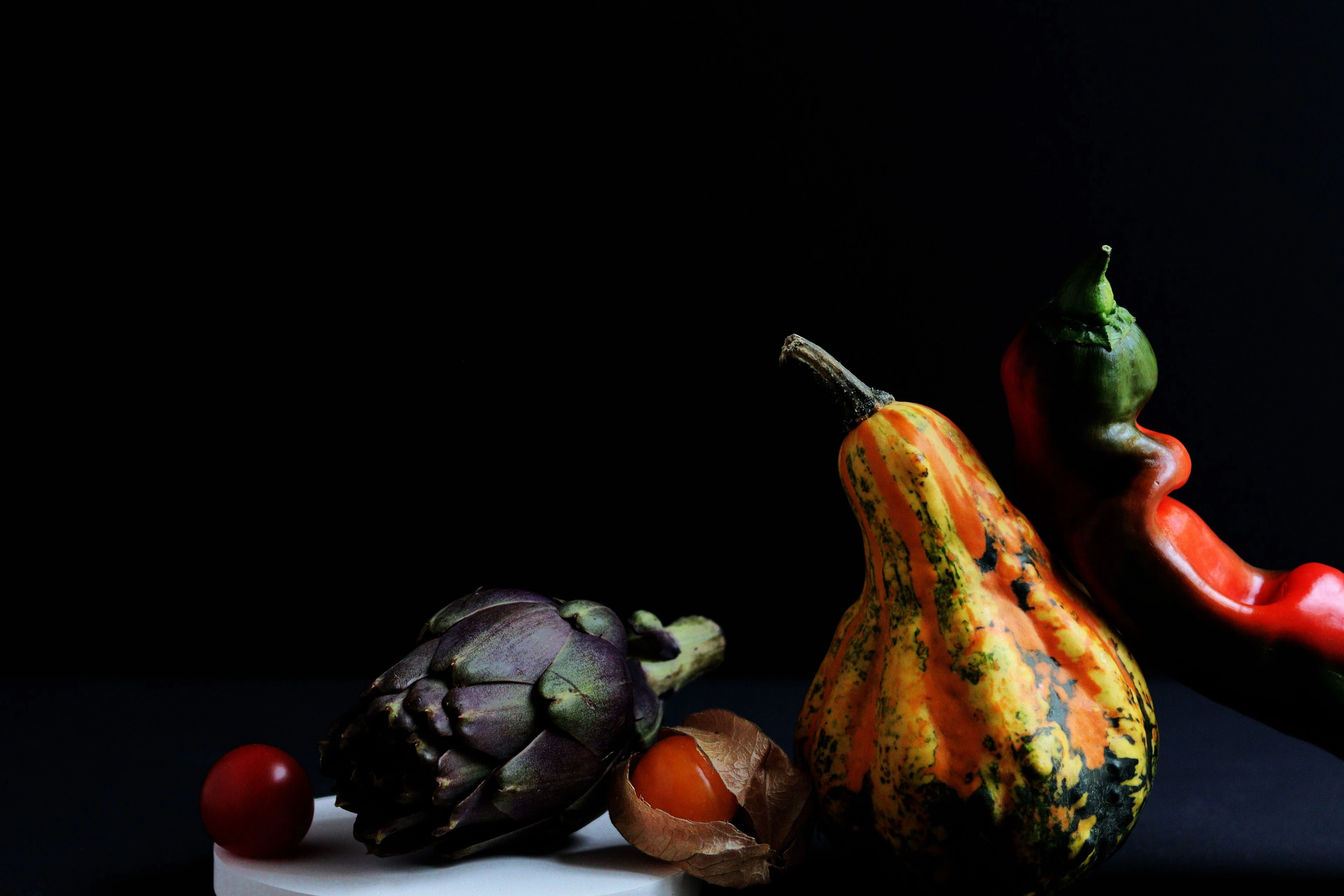 A still life of gourds and vegetables on black, lit low.