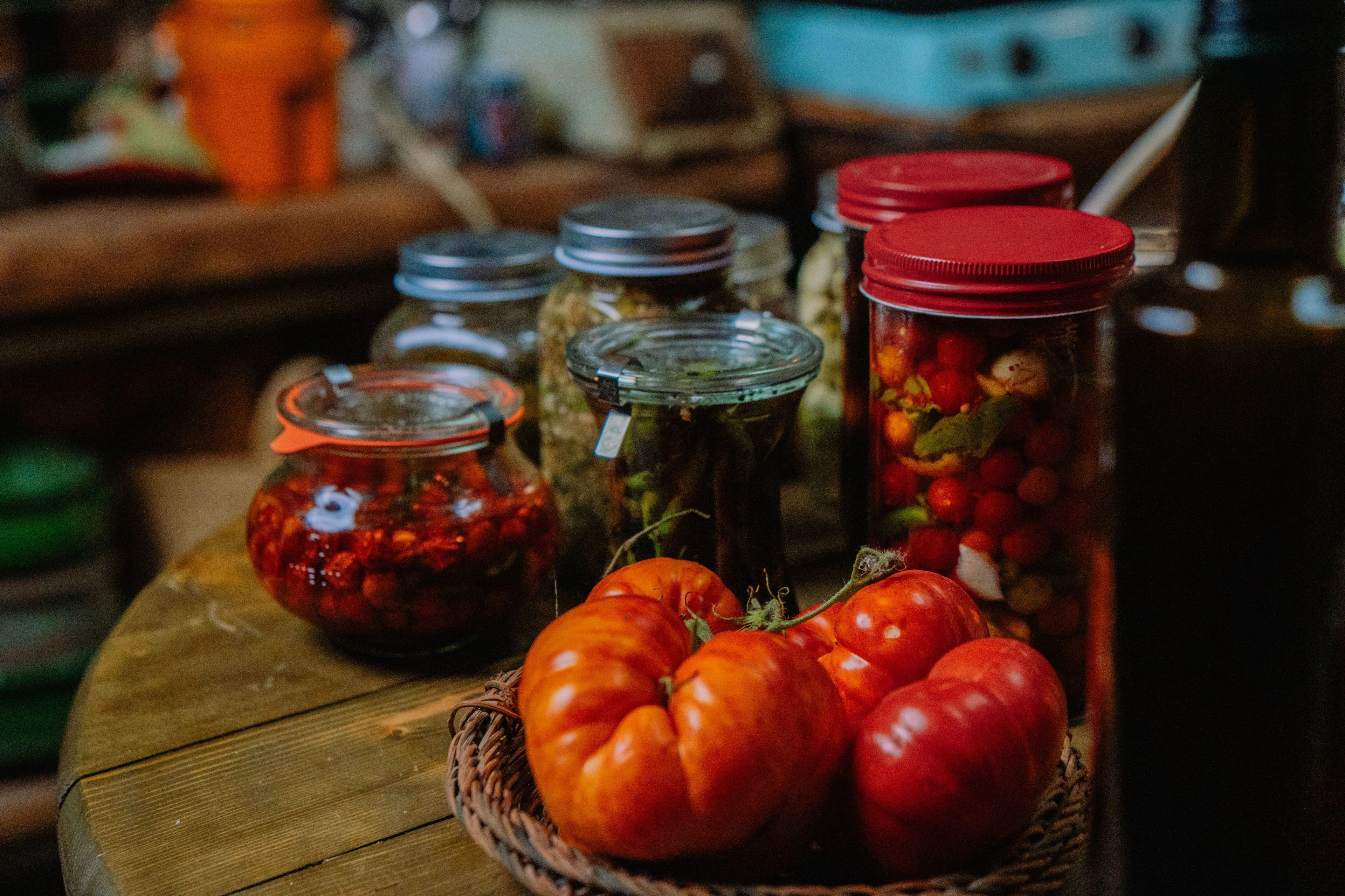 Jars of fermented vegetables and ripe tomatoes on a dark counter.