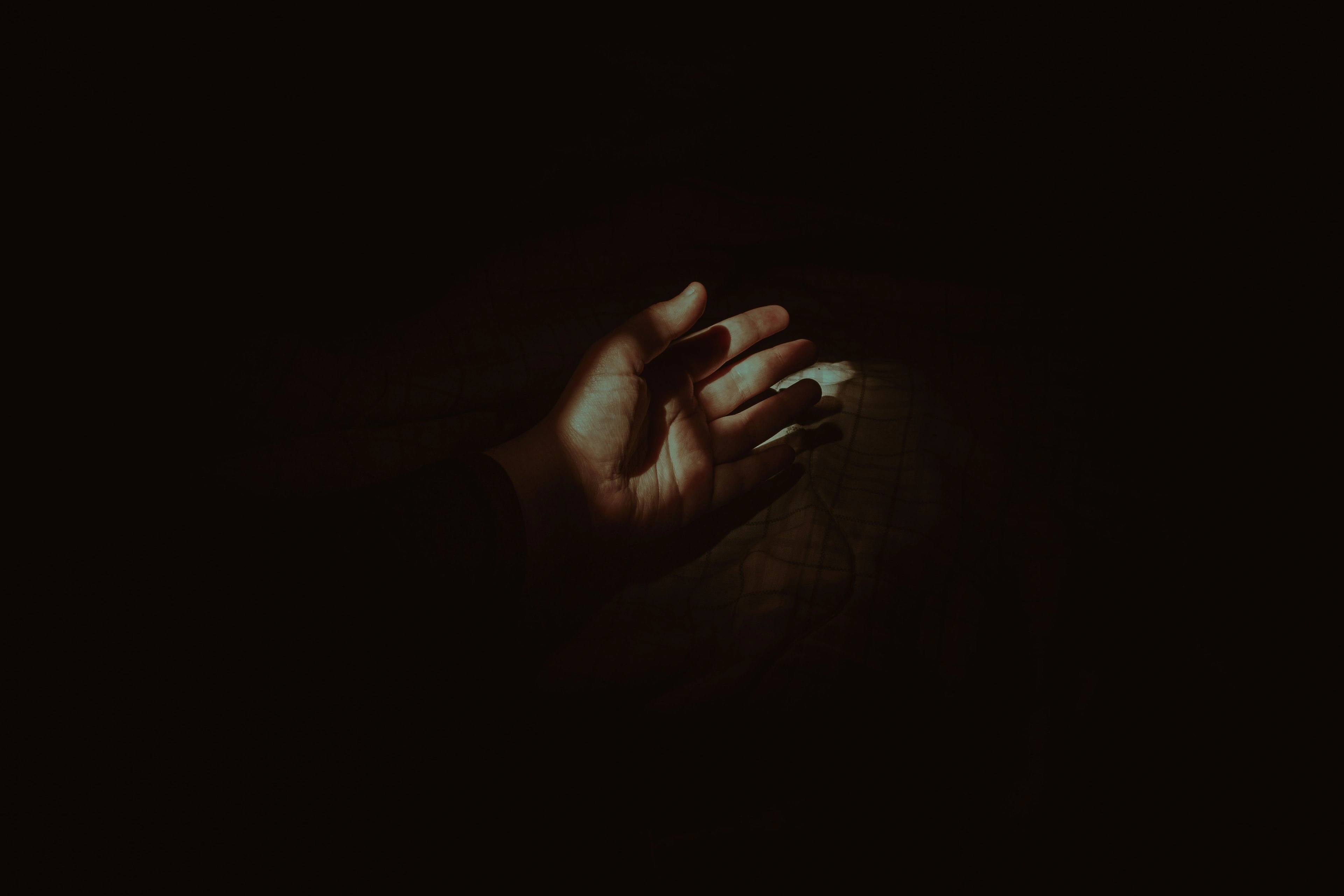 A child's open hand reaching into a shaft of dim light.