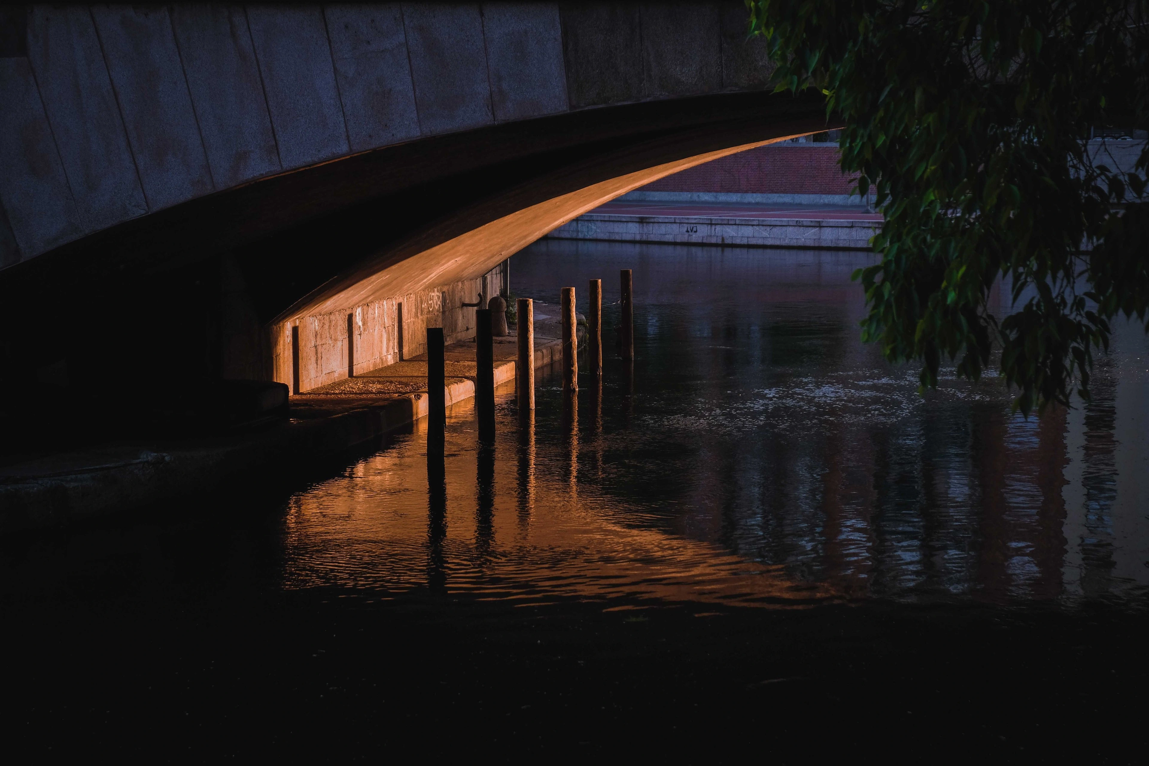 A dark curved footbridge reflected in still water at night.