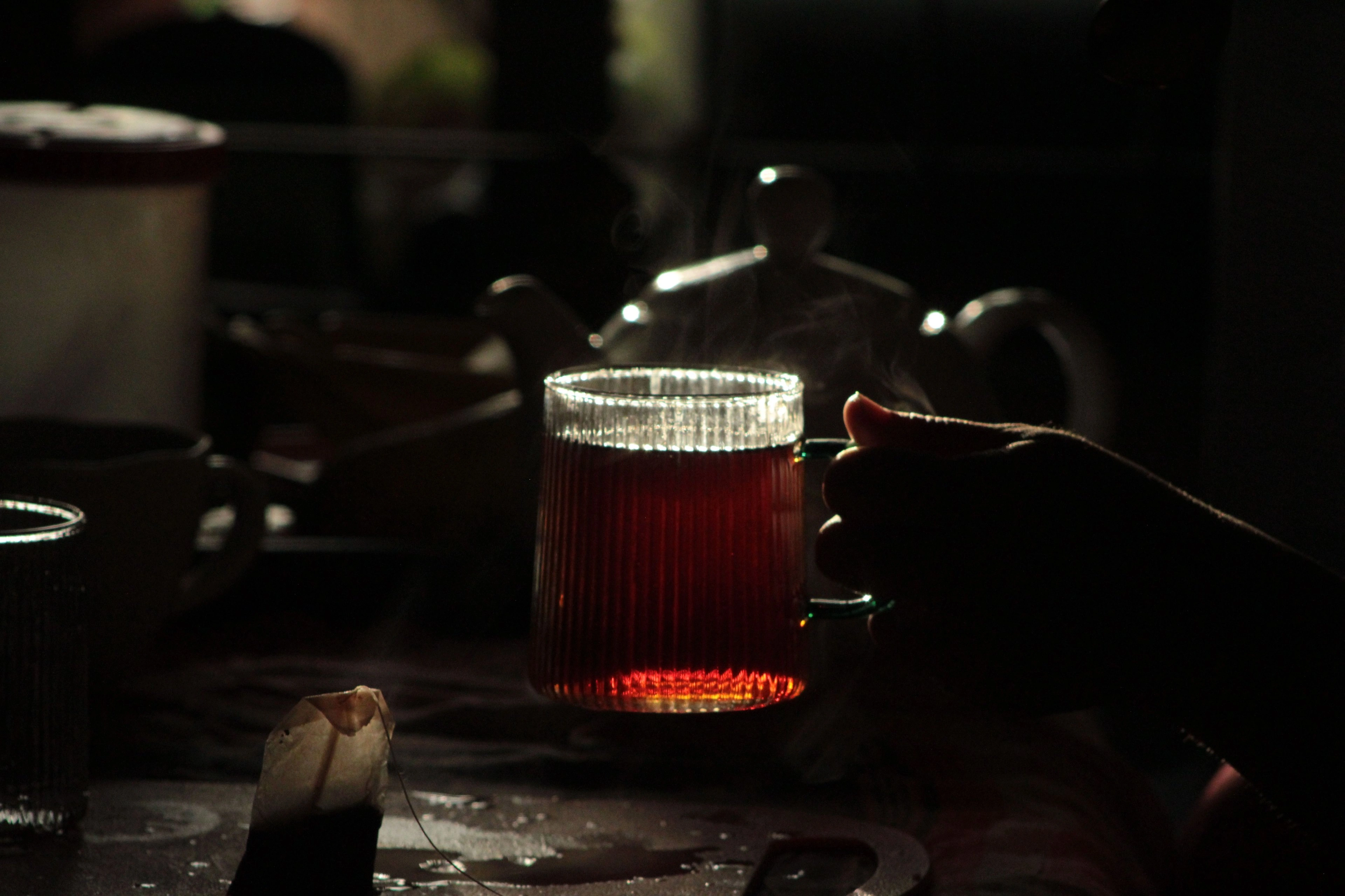 A glass of dark red tea with rising steam in low light.