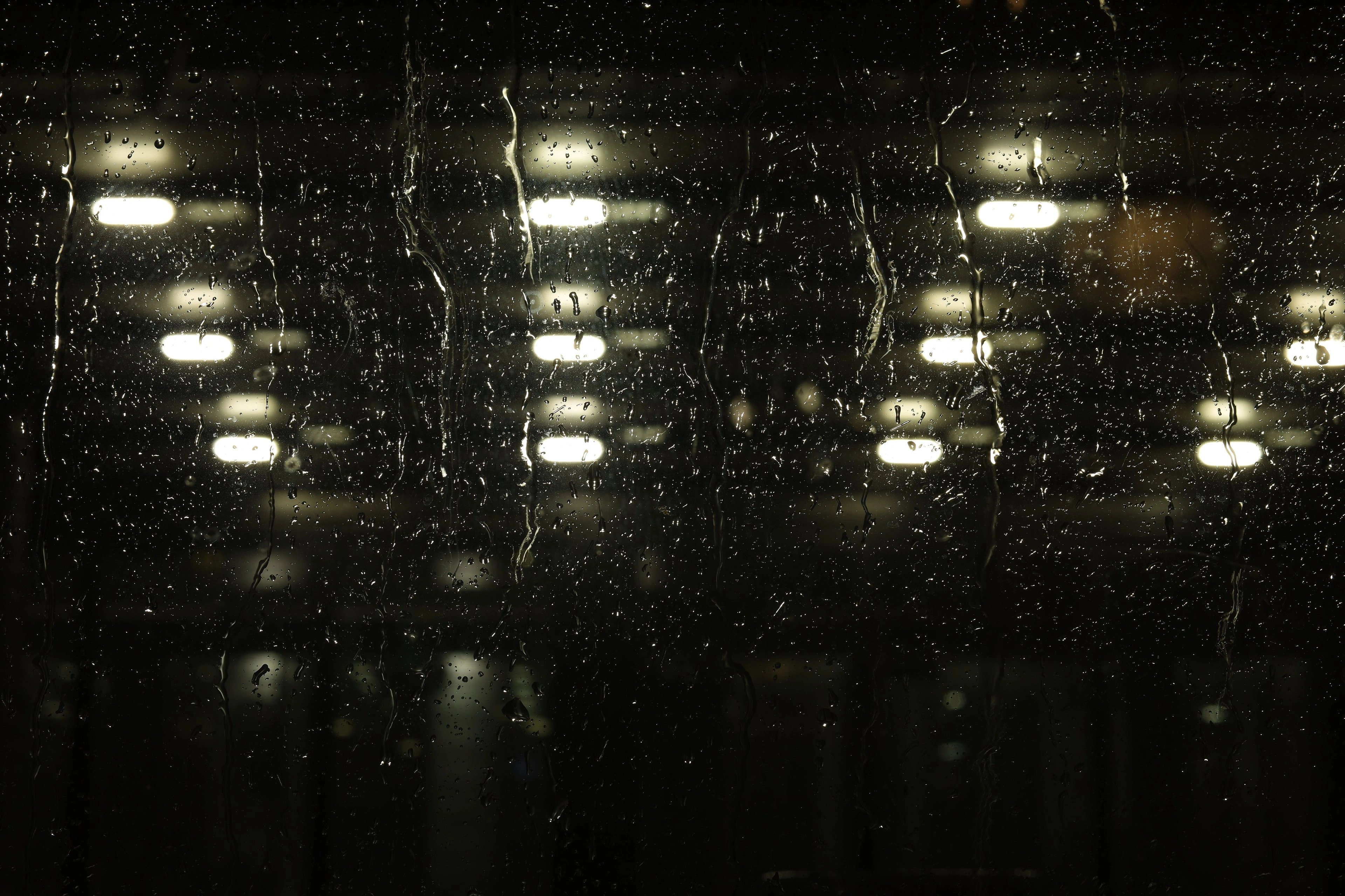 Rain running down a dark window with blurred city lights beyond.