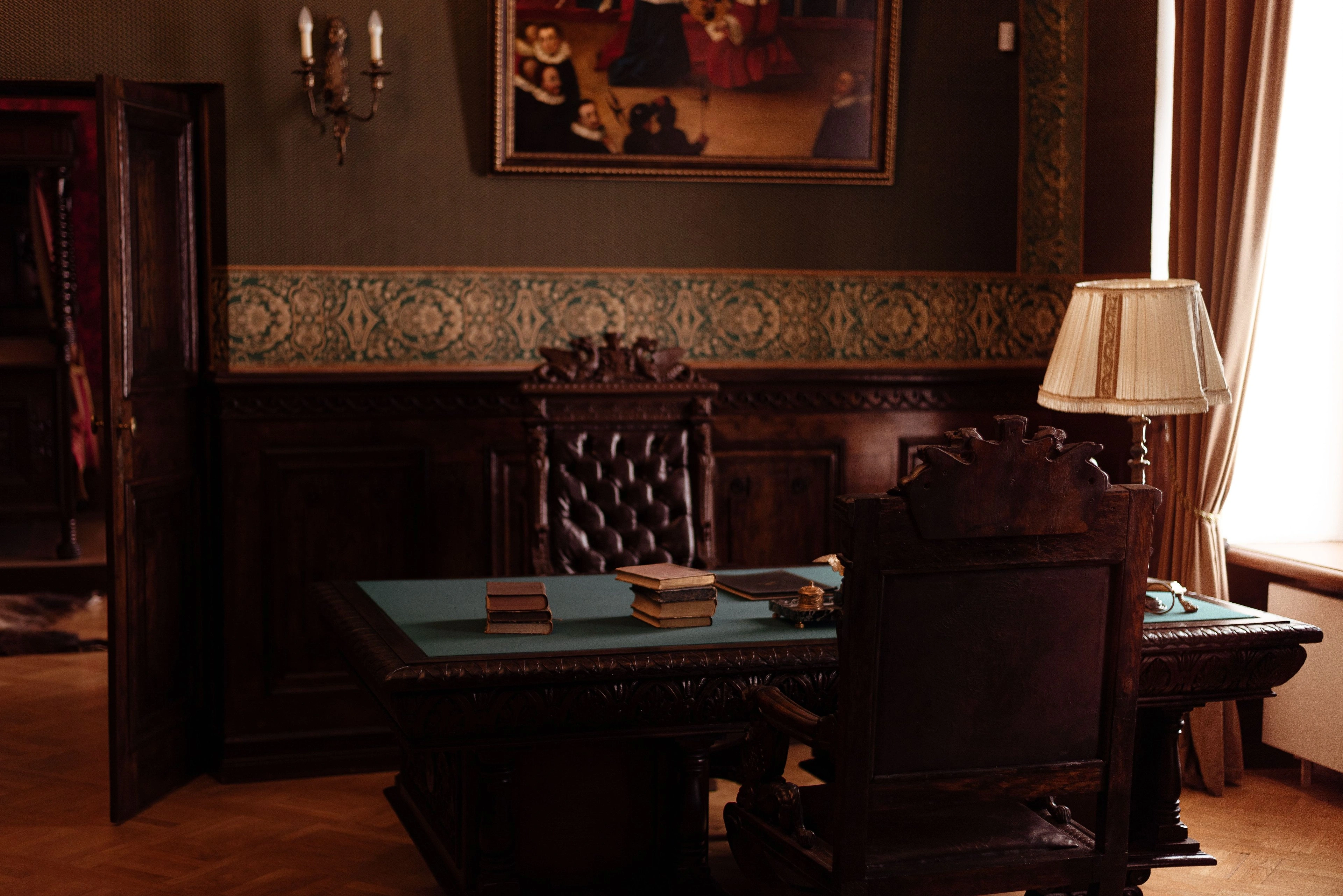An antique writing desk in a warmly lit, wood-paneled study.