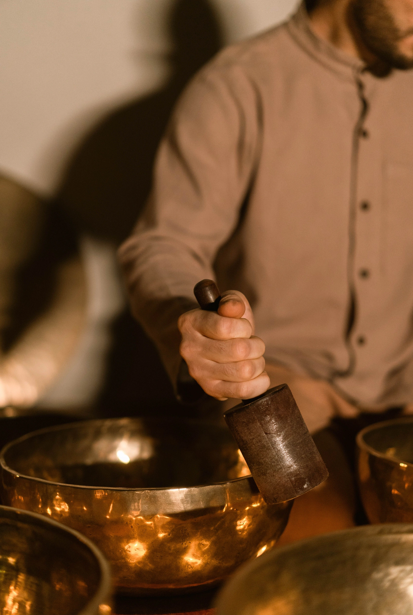 Hands grinding herbs beside brass singing bowls in warm light.