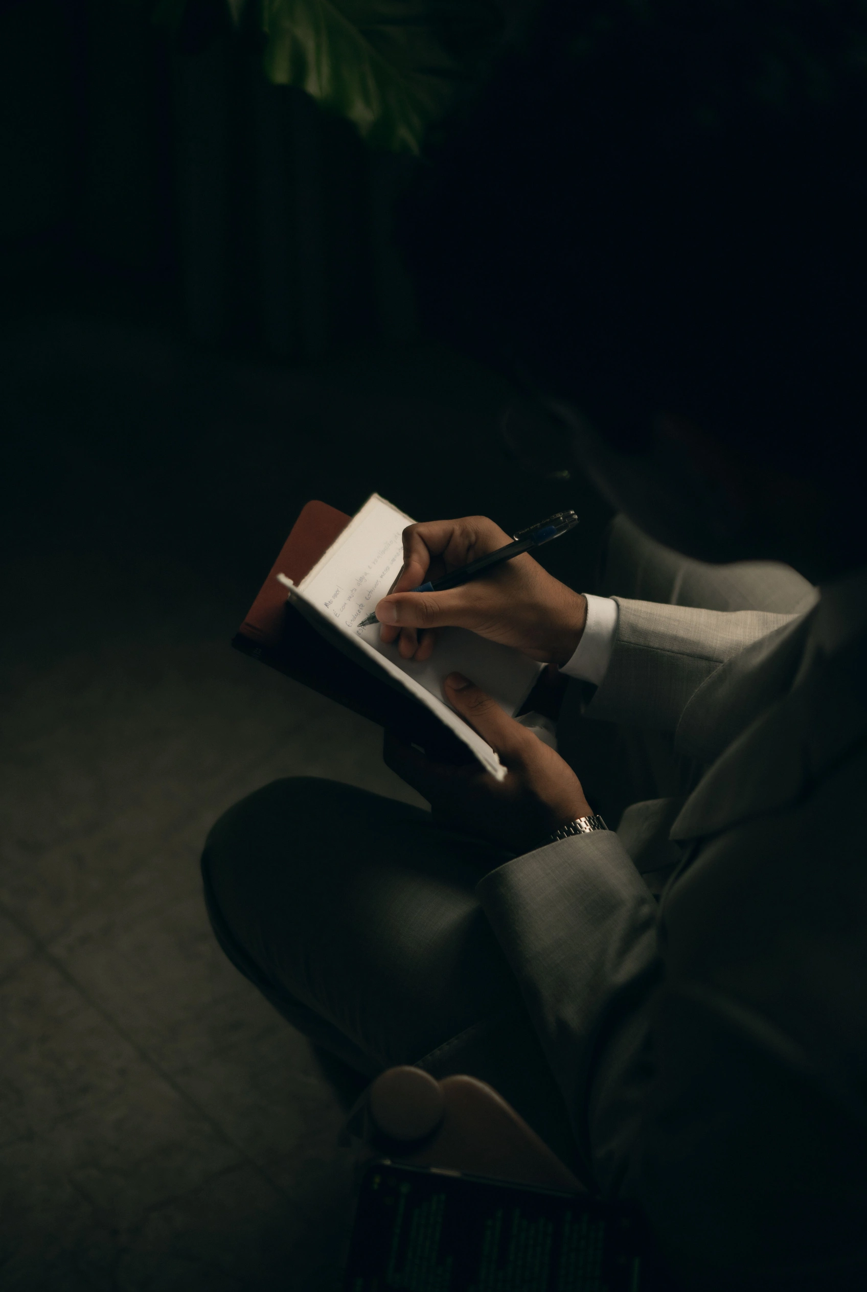 A figure writing in a journal by candlelight in the dark.