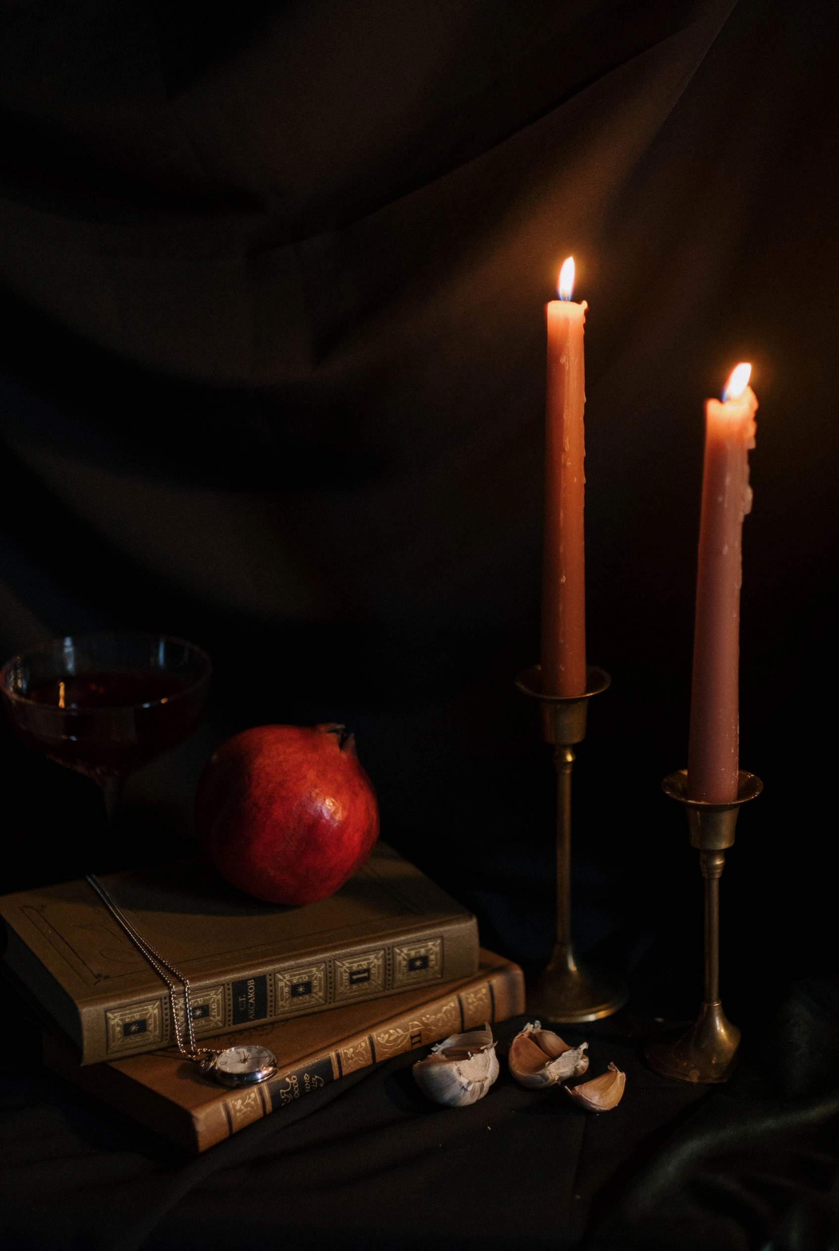 Two candles, old books and a pomegranate in a dark still life.