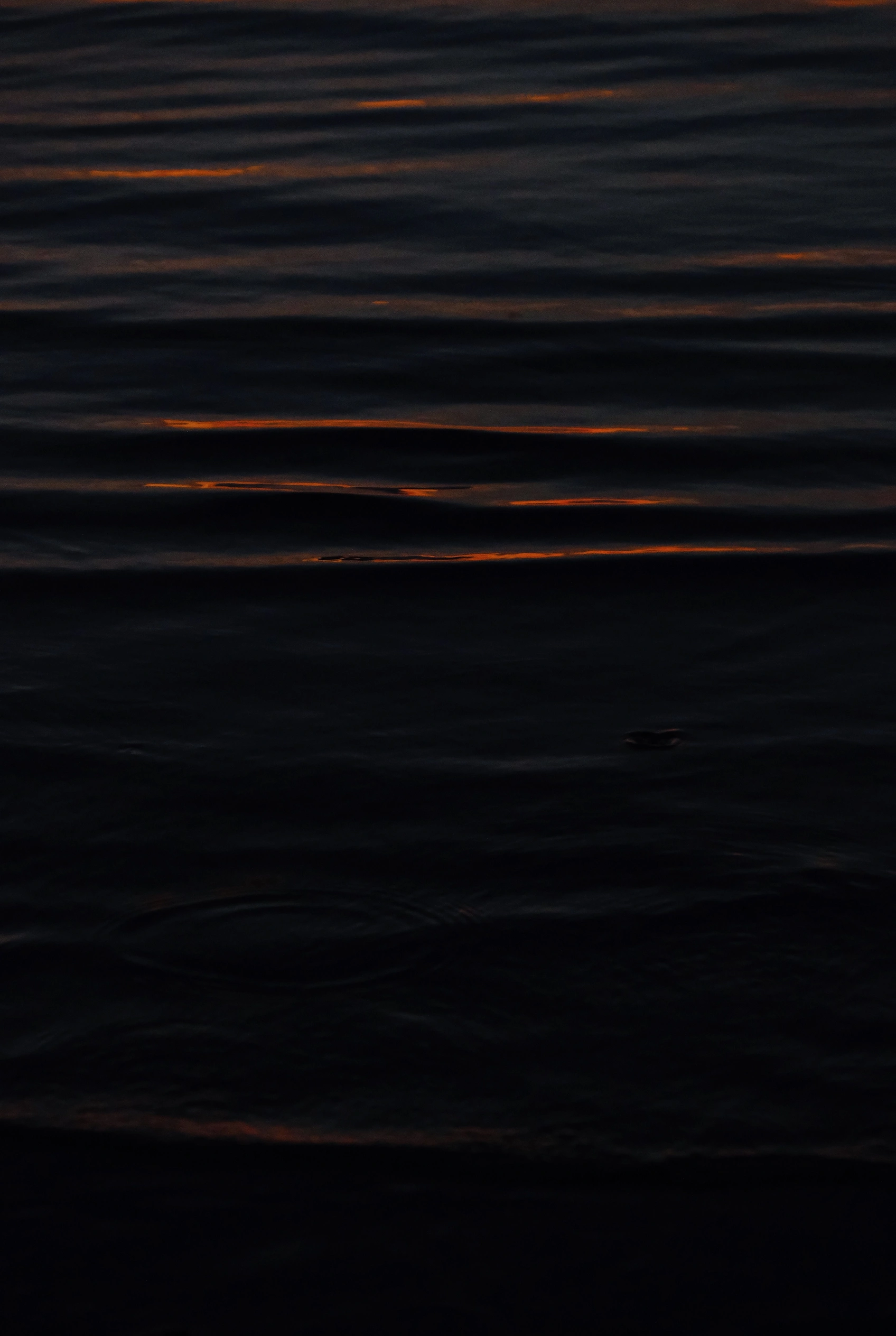 Bands of fading light across calm, dark water at dusk.