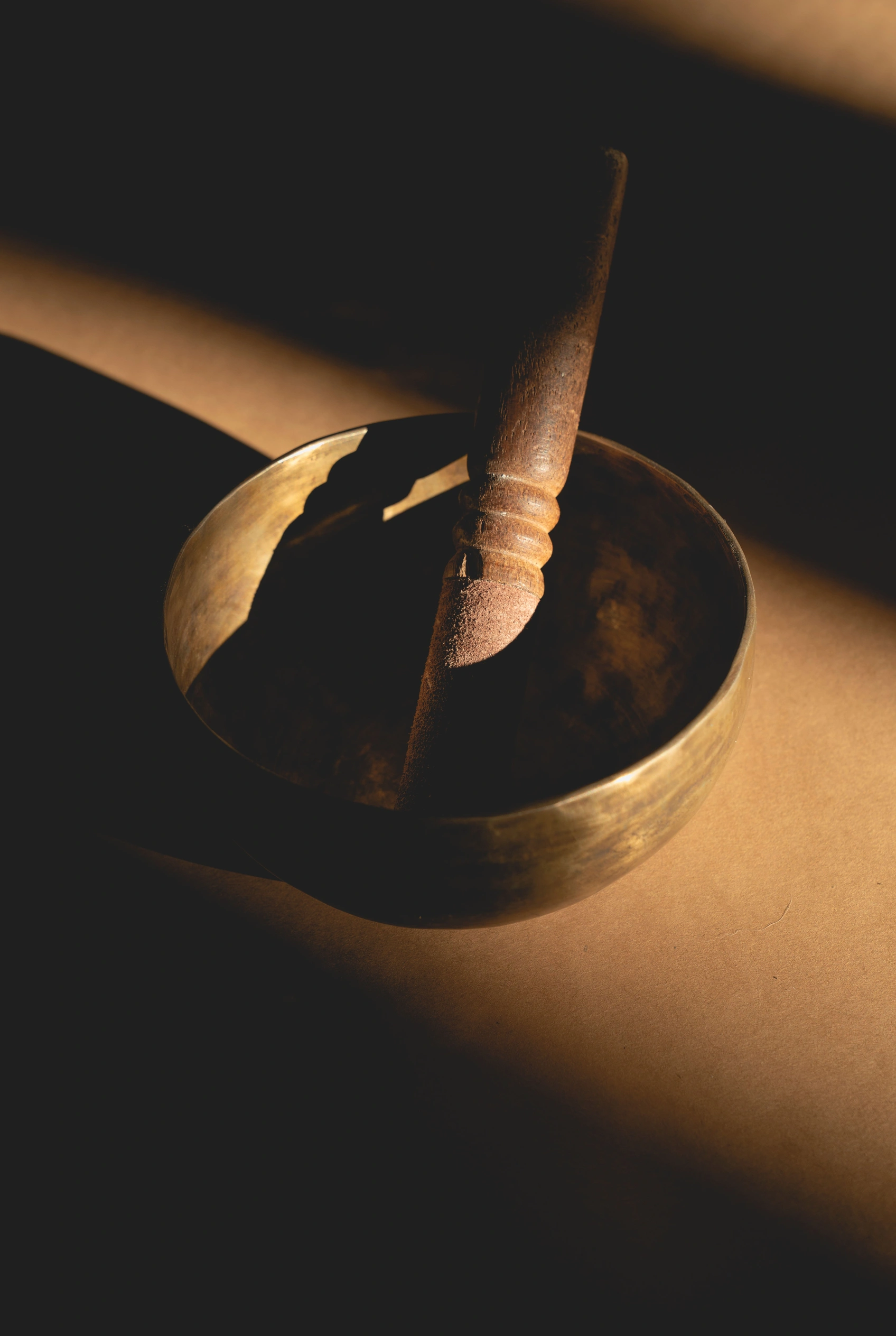 A brass singing bowl and mallet lit by warm gold light.