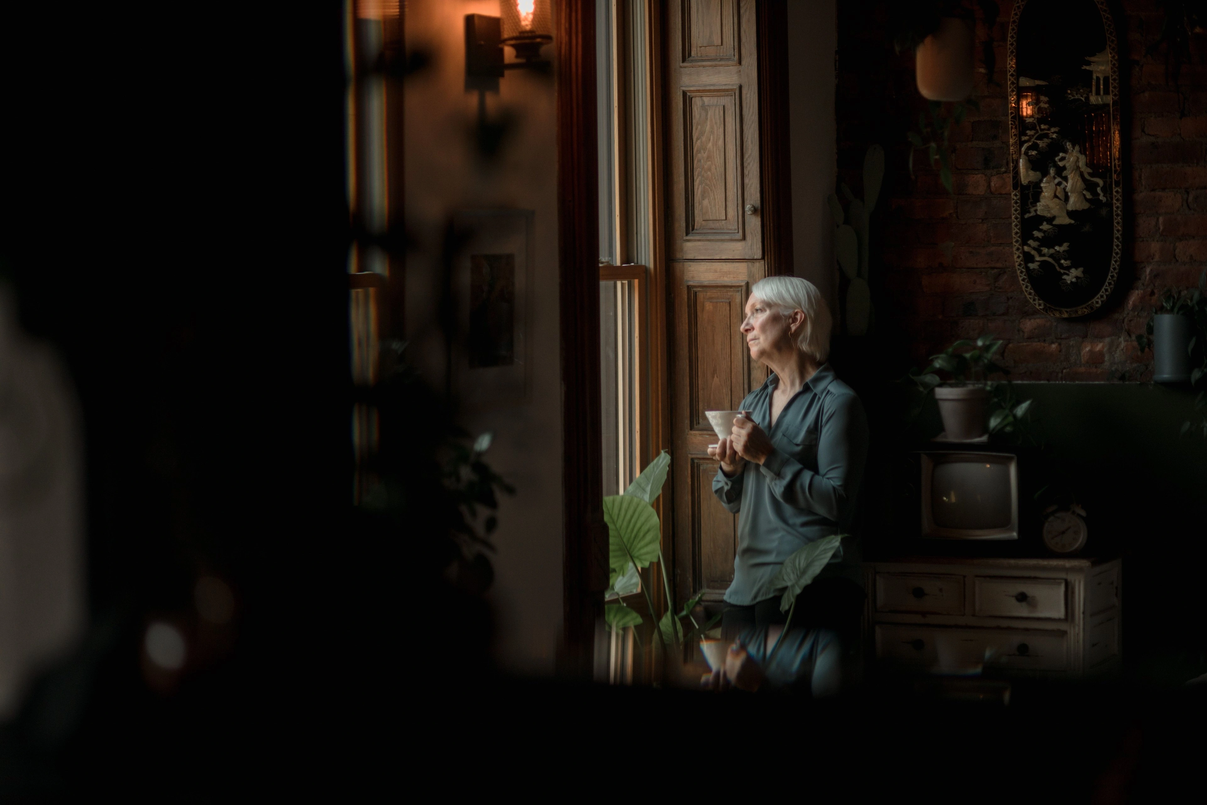 A person standing by a bright window in a warm, dim room.
