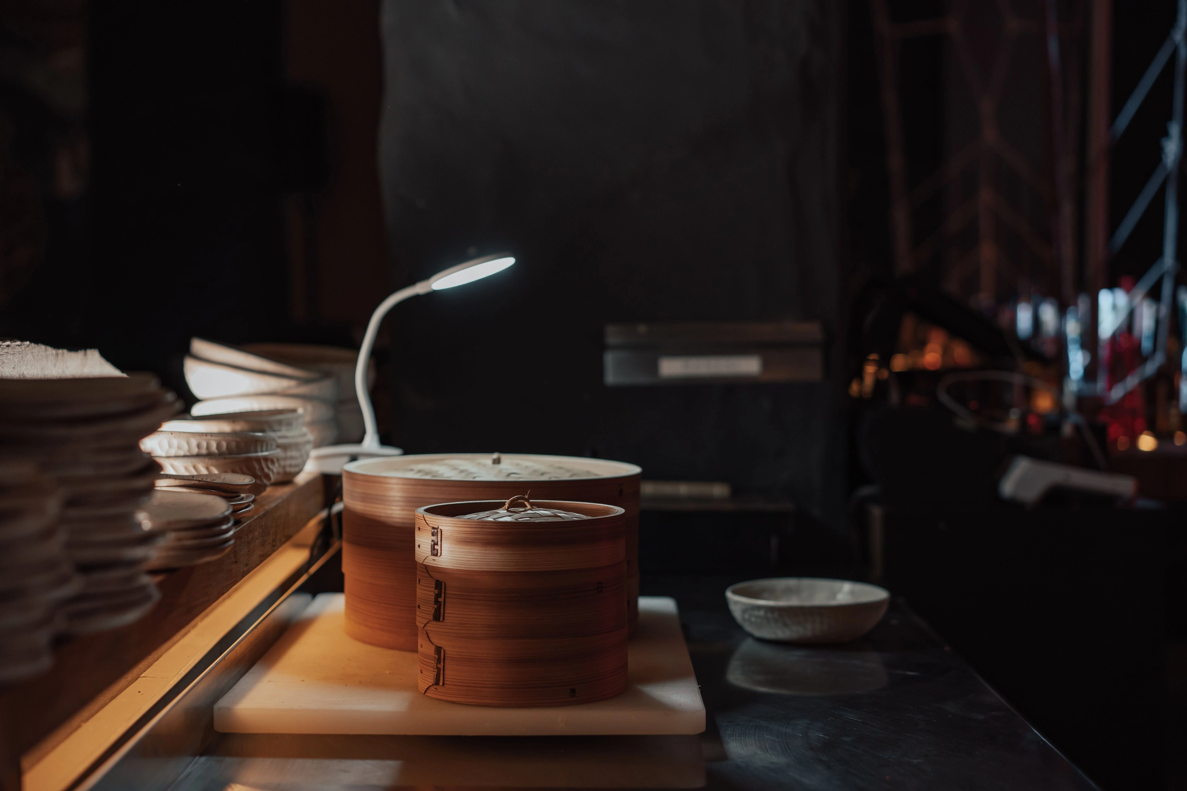 A bamboo steamer releasing steam under a small lamp in a dark kitchen.