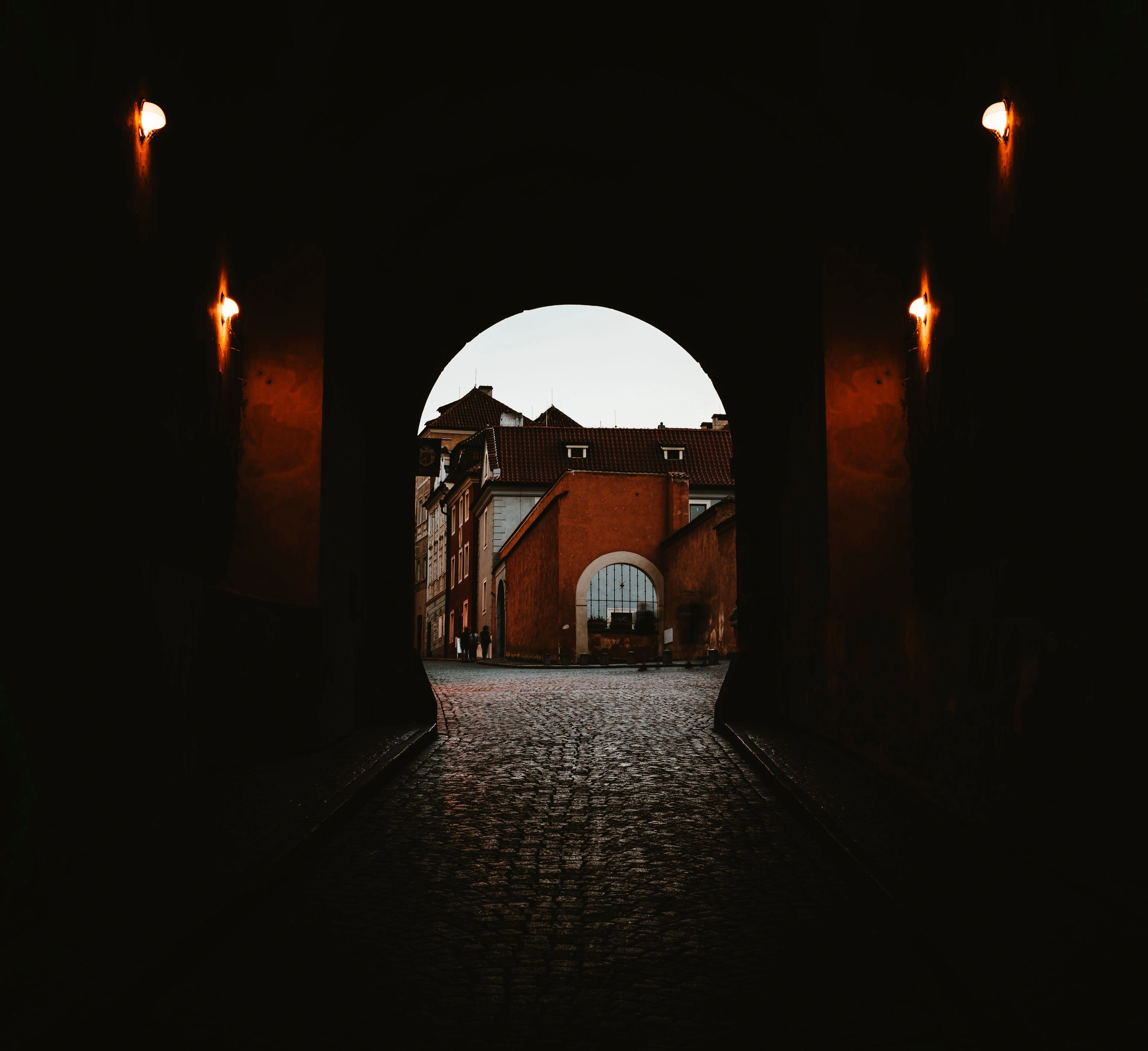 A dark stone archway opening onto a torchlit courtyard beyond.