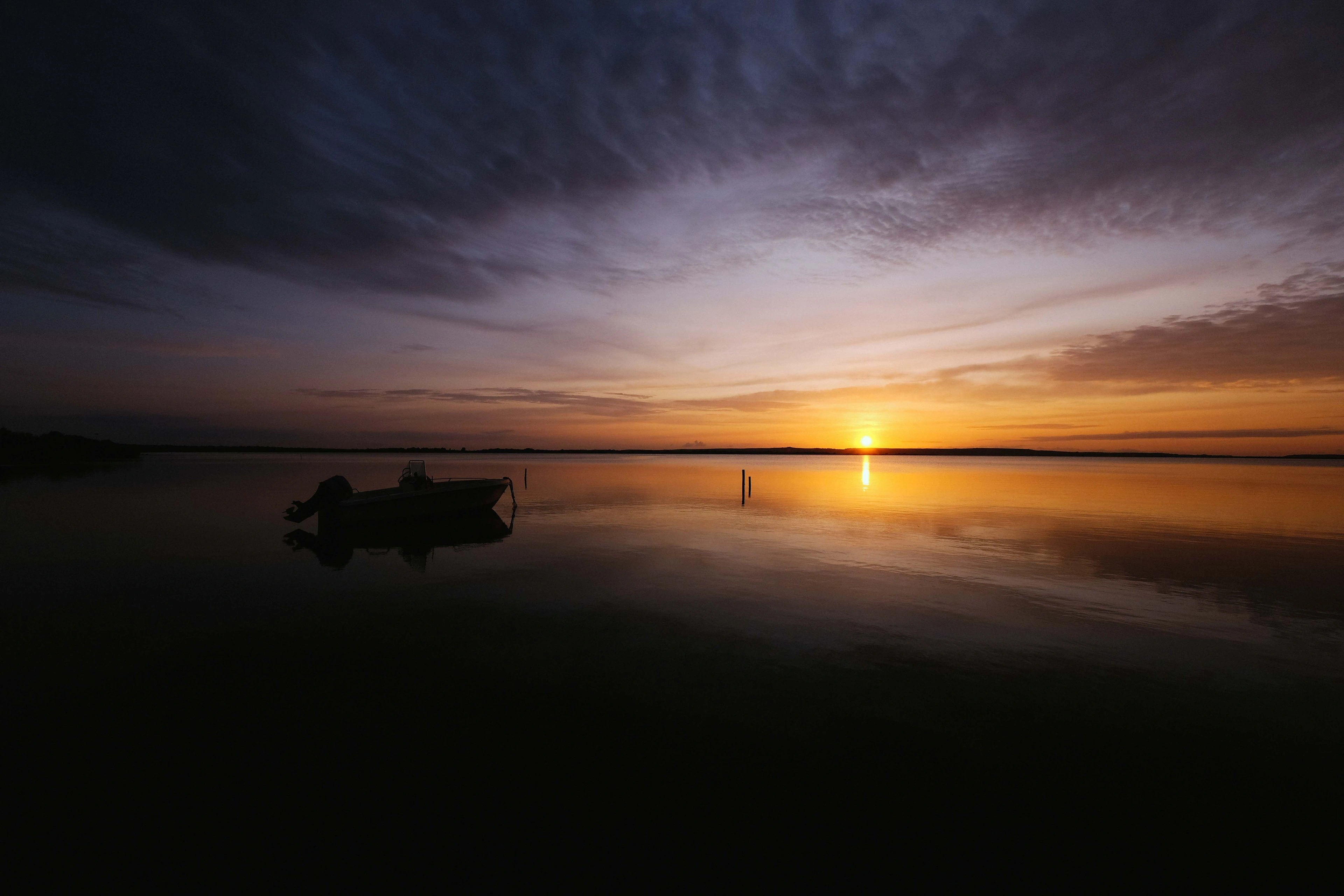 The sun low over calm water at dawn, a small boat in silhouette.