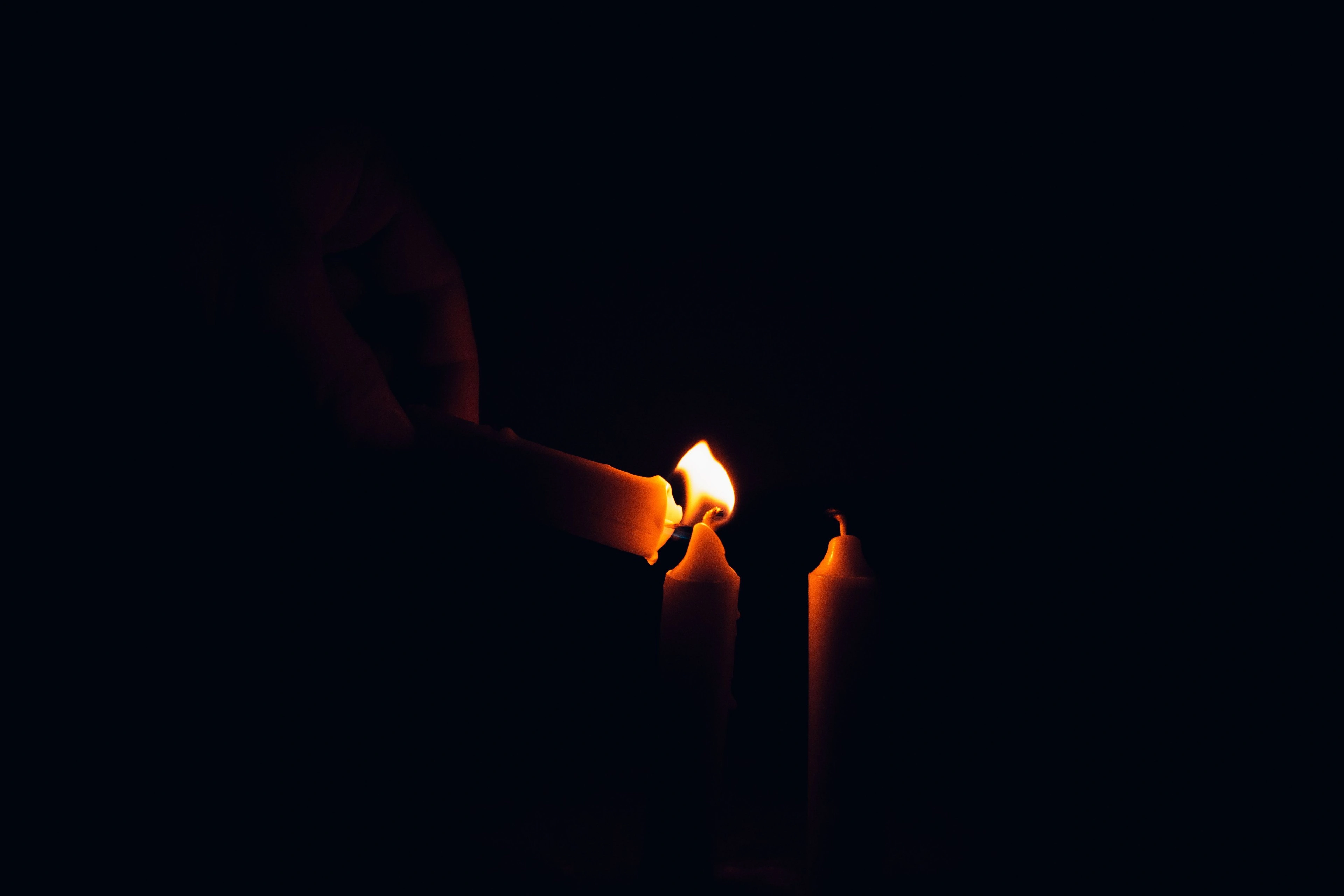 A hand cupped around a small candle flame in deep darkness.