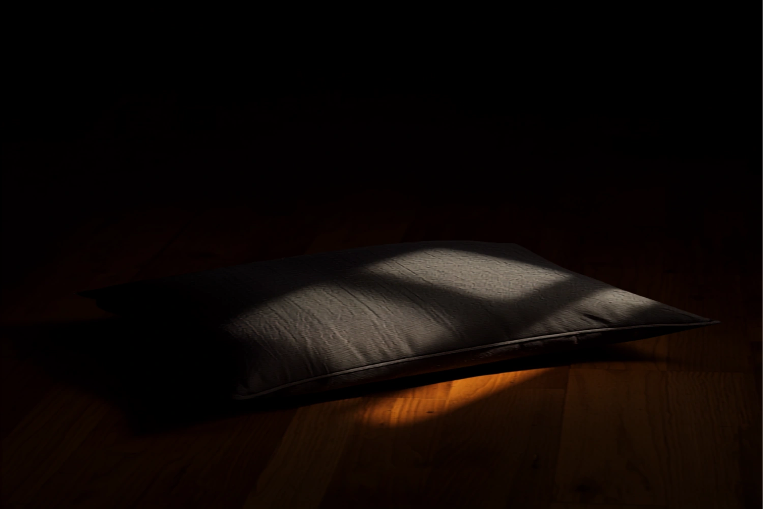 A soft indented cushion of dark linen catching a shaft of warm gold light, evoking stillness before release.