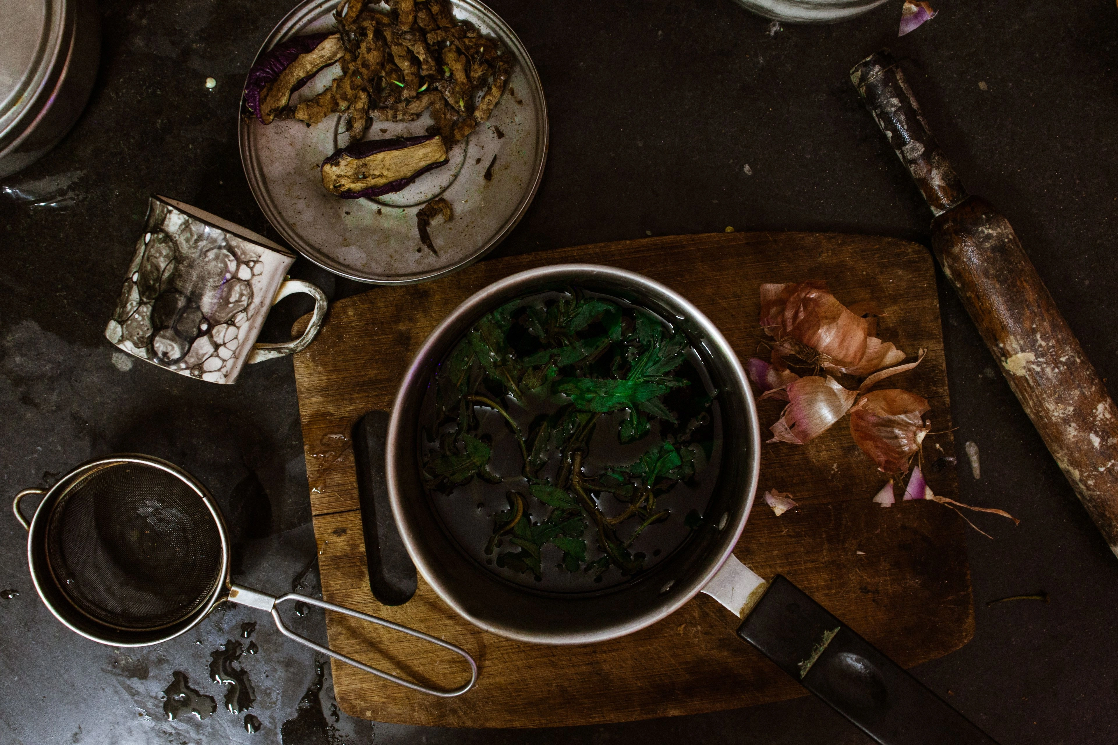 An overhead view of a pot of greens and bowls on a dark table.