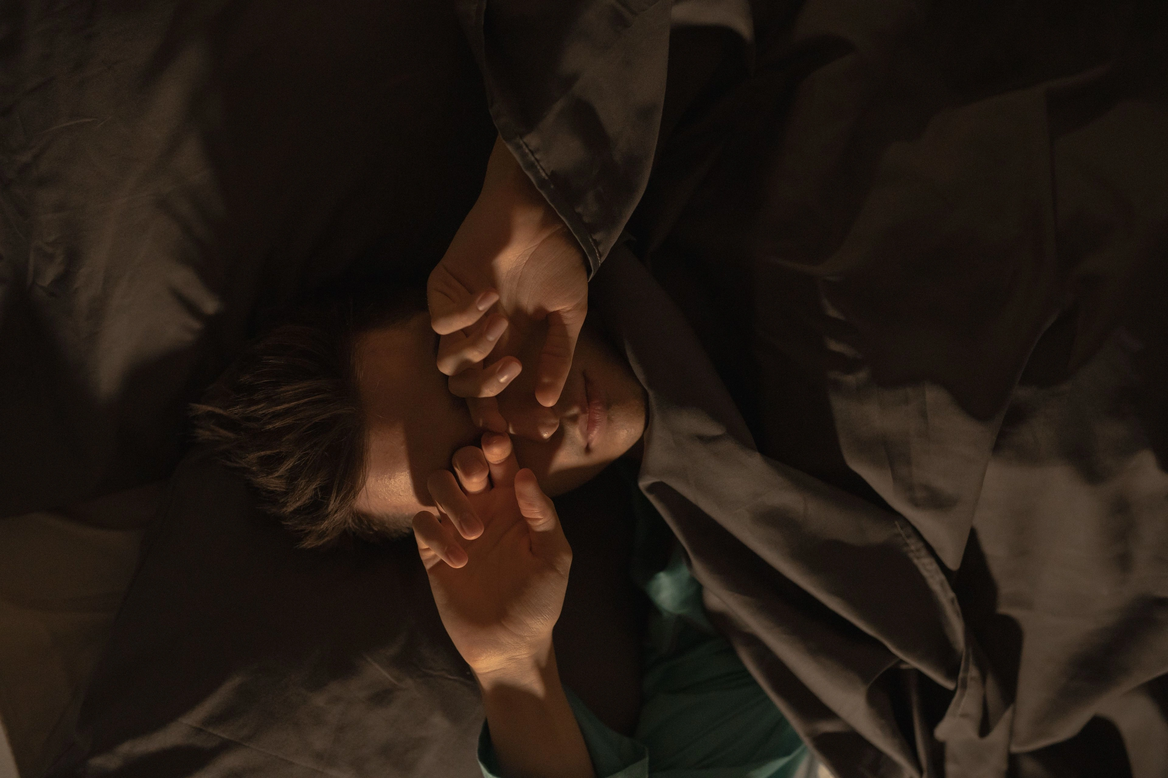 Hands resting under a heavy blanket in a dim bedroom.