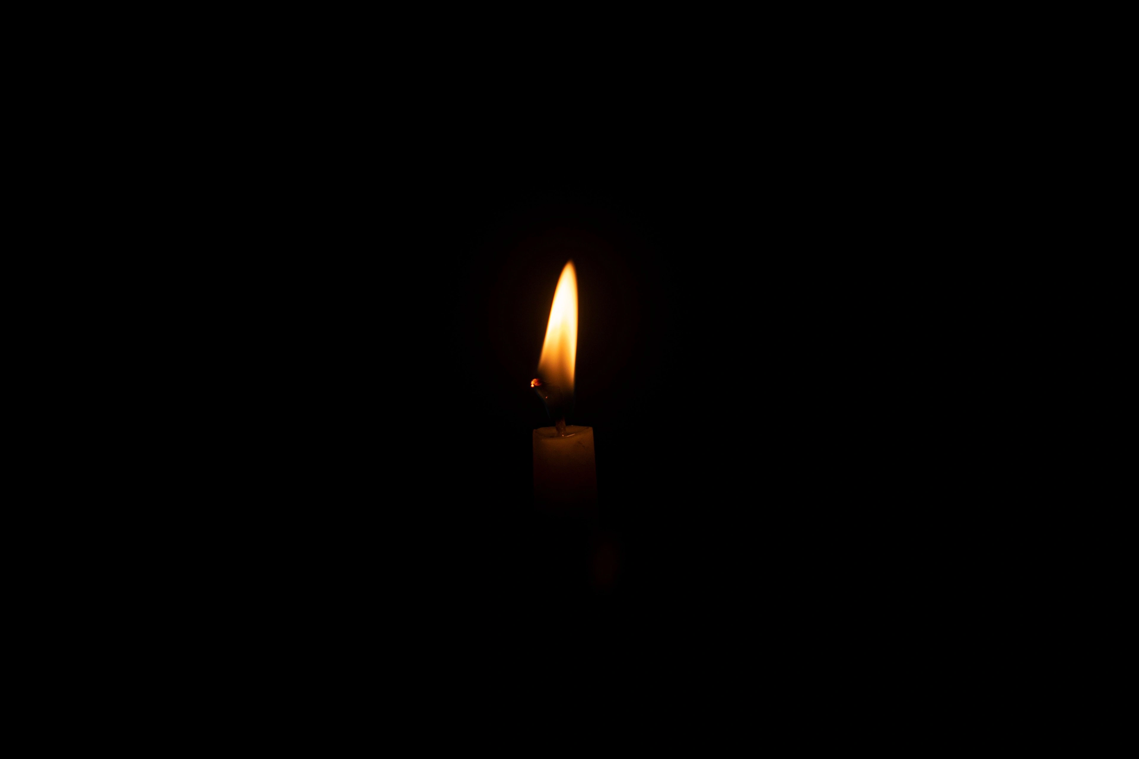 A single candle flame glowing softly against darkness.