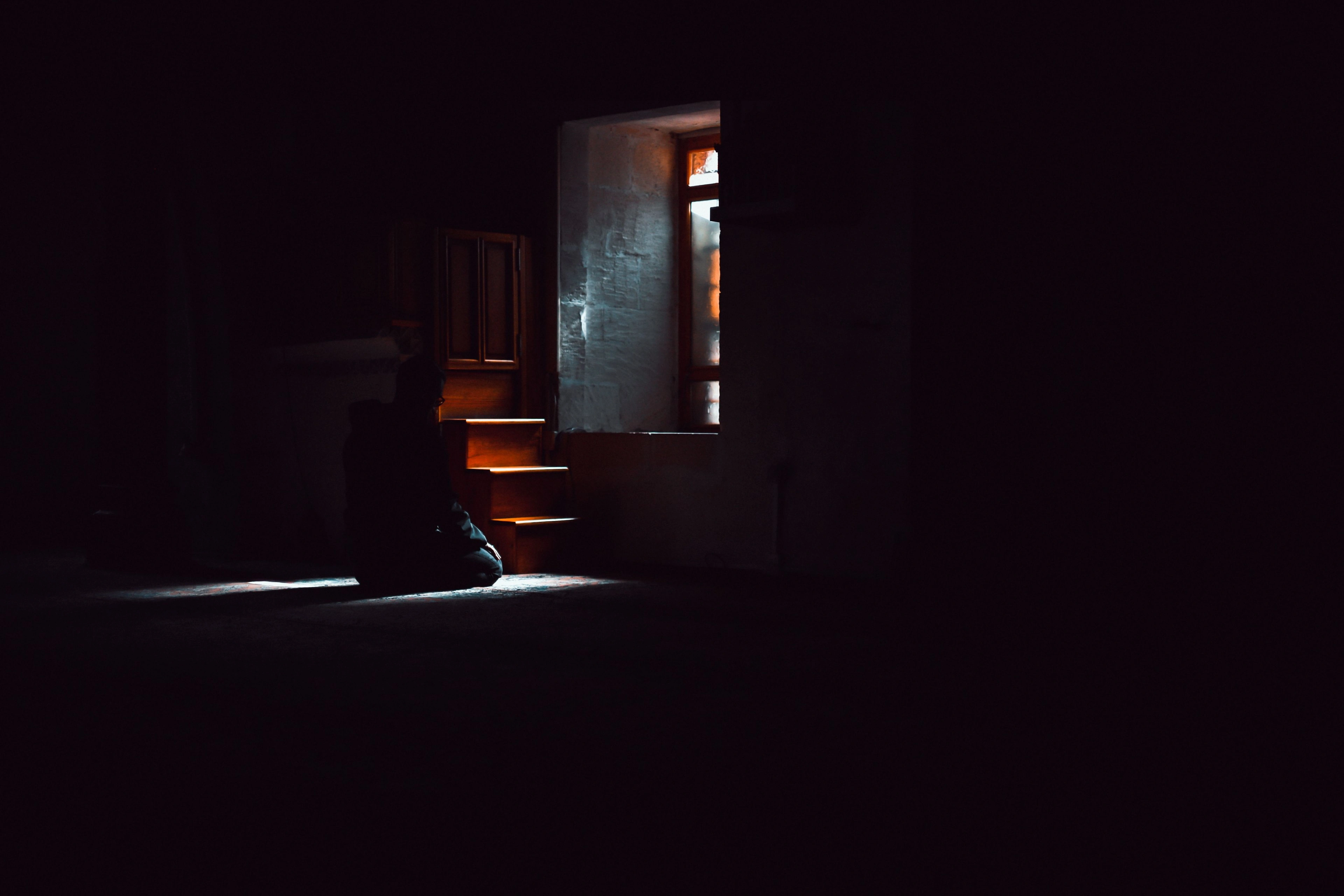A figure crouched in a dark room lit by a single doorway of light.