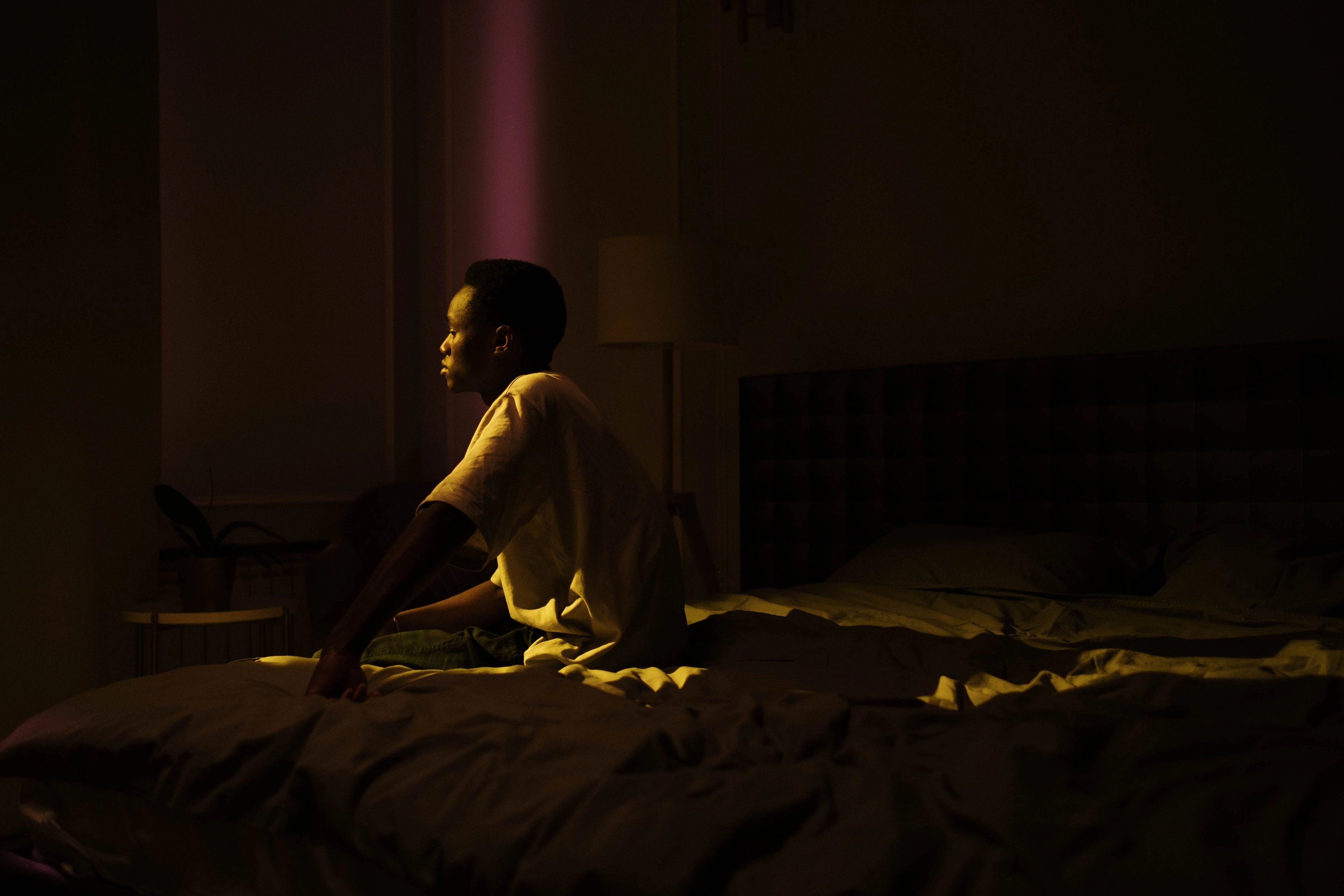 A person sitting on the edge of a bed in a dark bedroom at night.
