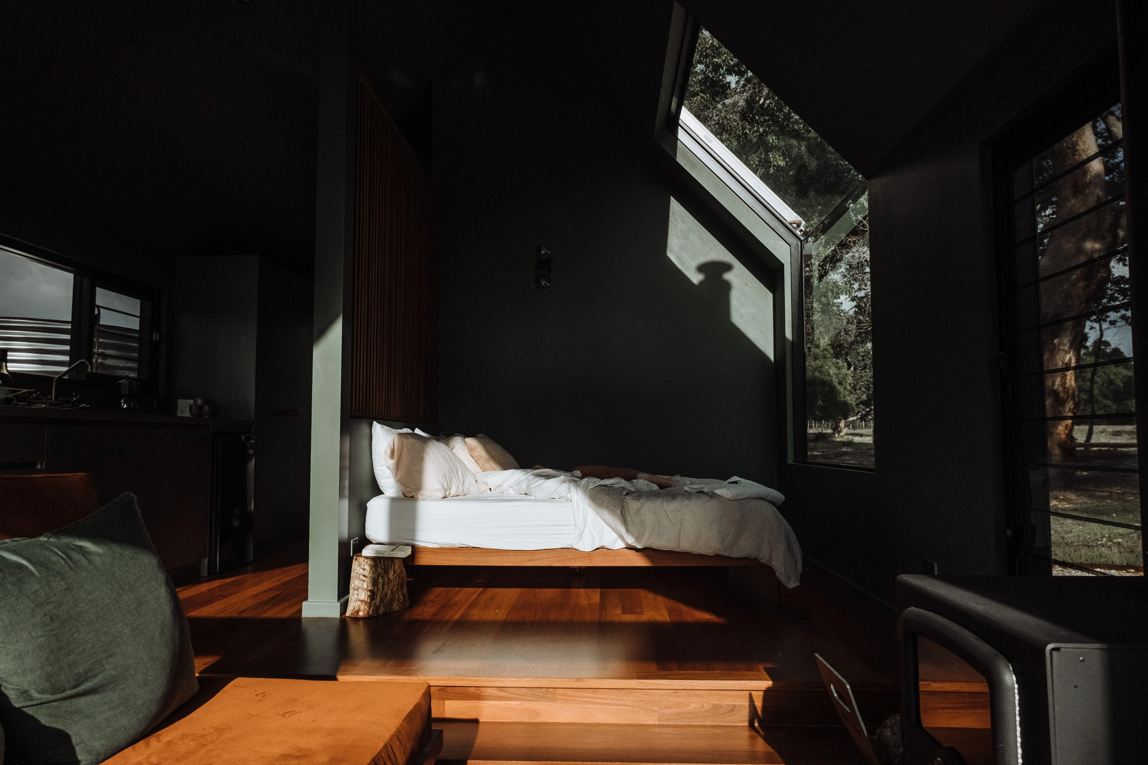 A neatly made bed by a window in a dark, warm cabin room.